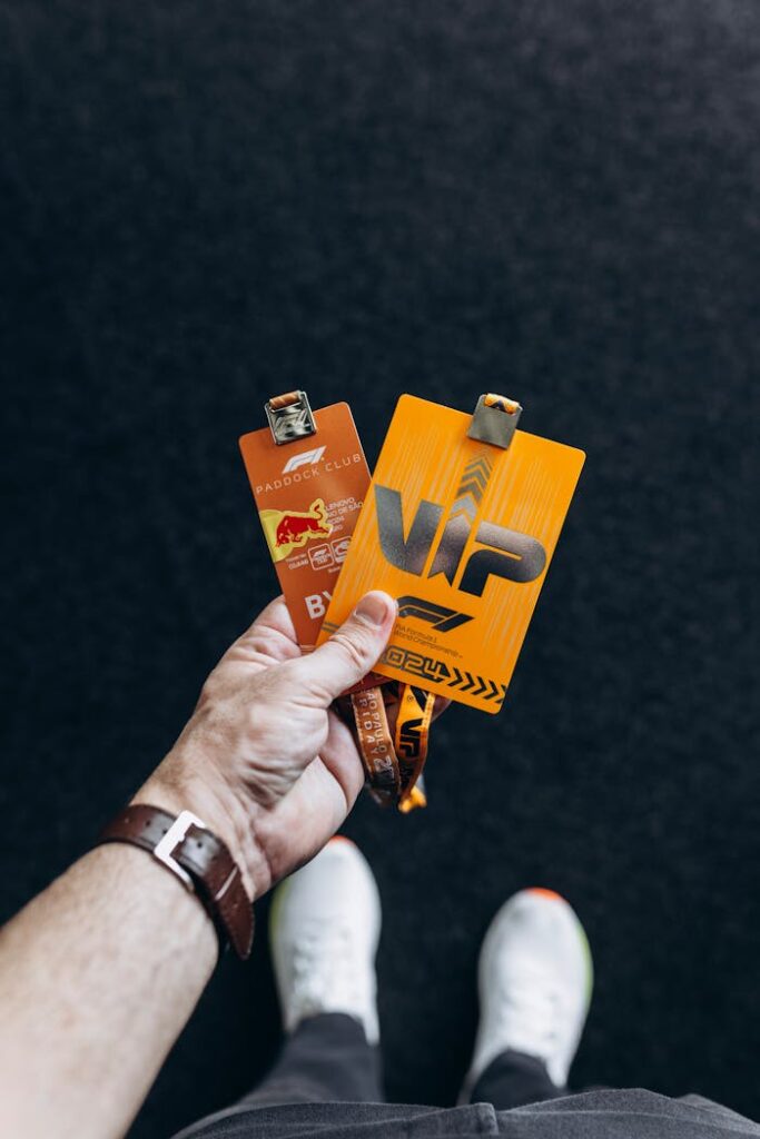 Close-up of a hand holding two VIP event badges against a black background.